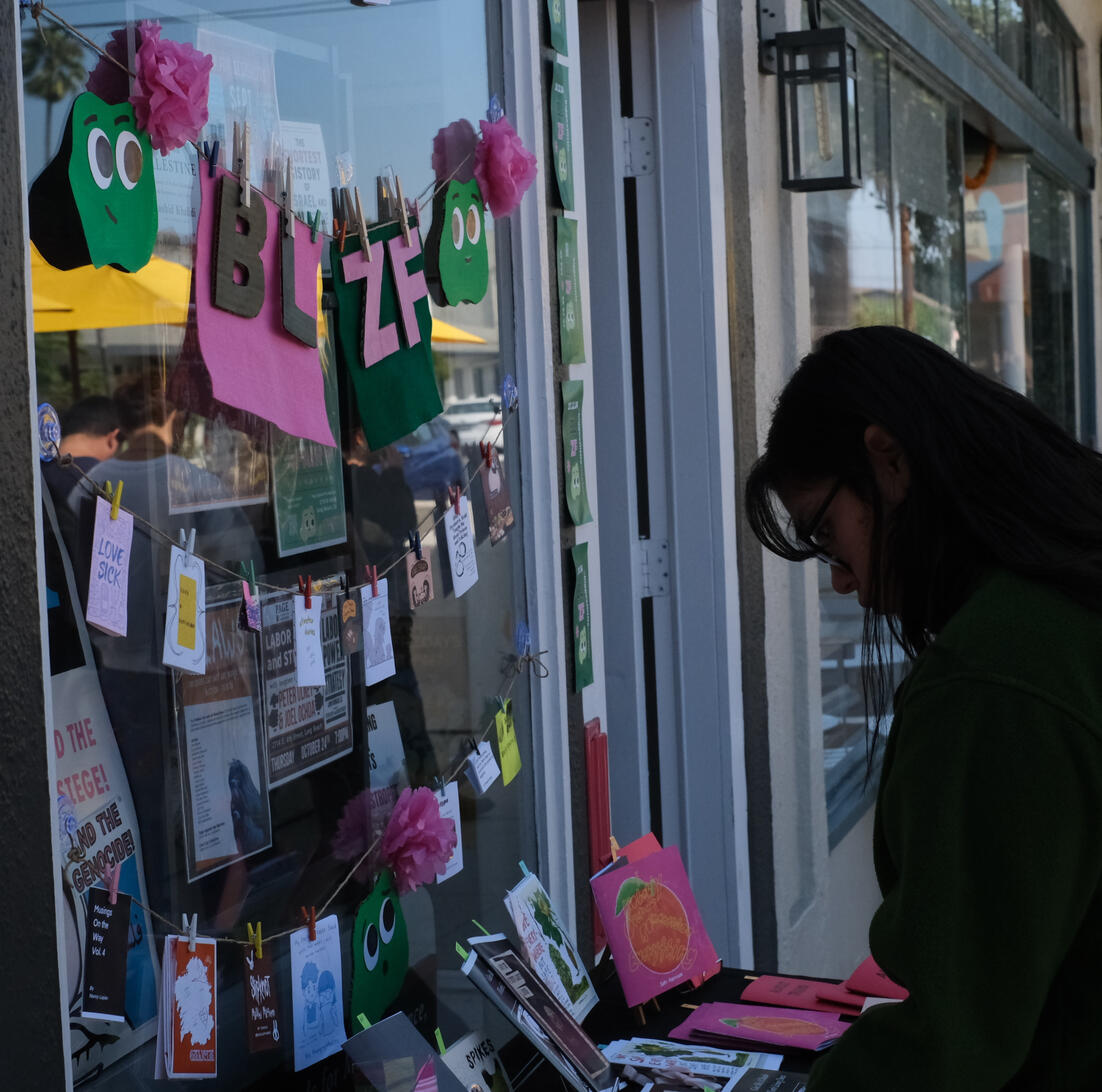 A customer at the first Biggest Little Zine Fair, in October 2024, Long Beach, CA. Including the BLZF zine display window.